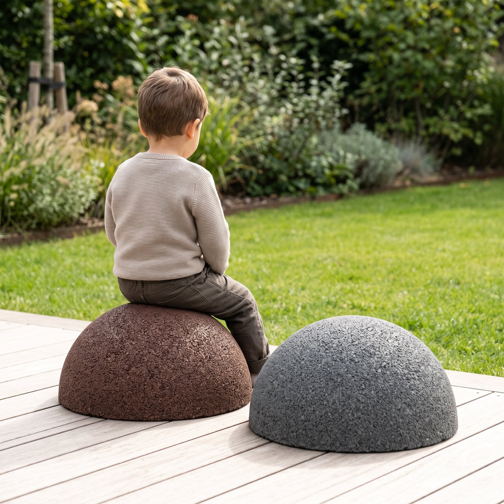 Enfant assis sur une demi-sphère marron, à côté d'une demi-sphère gris anthracite, sur une terrasse — visuel d'illustration