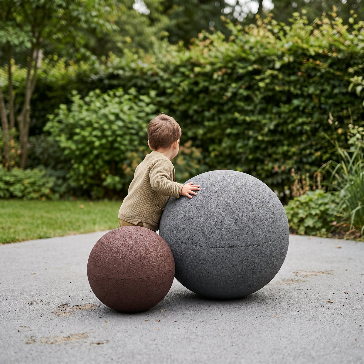 Enfant jouant avec deux sphères de jeu en granulat de semelles recyclées, gris anthracite et marron — visuel d'illustration